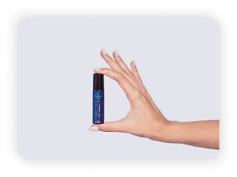 A bottle of Shunyata Migraine Relief Roll On held by a hand model against a plain backdrop