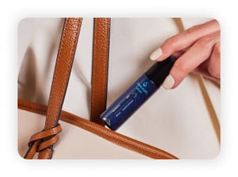 A bottle of Shunyata Migraine Relief Roll On held by a hand model going inside a hand bag